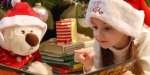 girl and bear in holiday hats reading a book