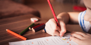 young child writing with a red pencil back to the routine