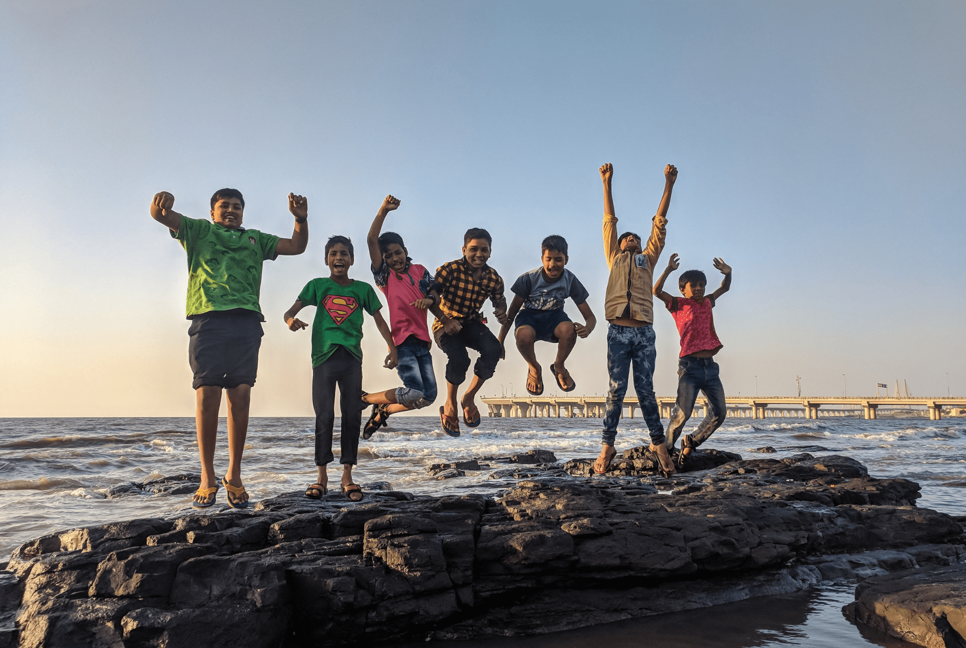 kids jumping together on a rock near the ocean celebrating Earth Day