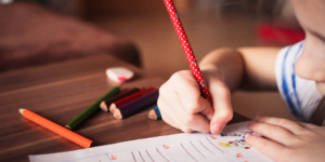 child using right hand to write with a red pencil