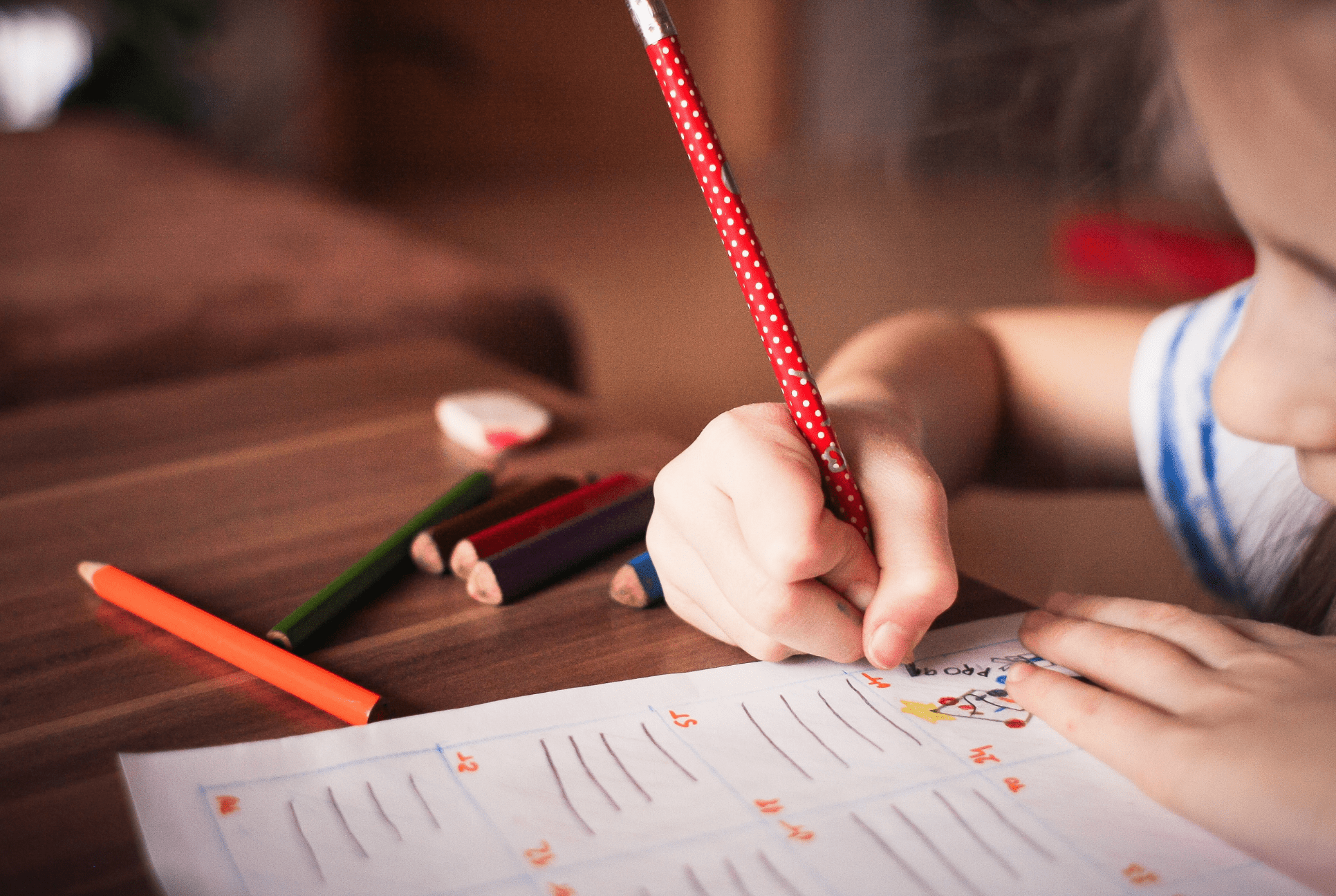 child using right hand to write with a red pencil