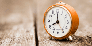 orange clock on a wood table end of daylight savings survival guide