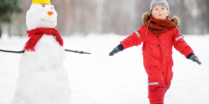 boy in red snow suit next to snowman