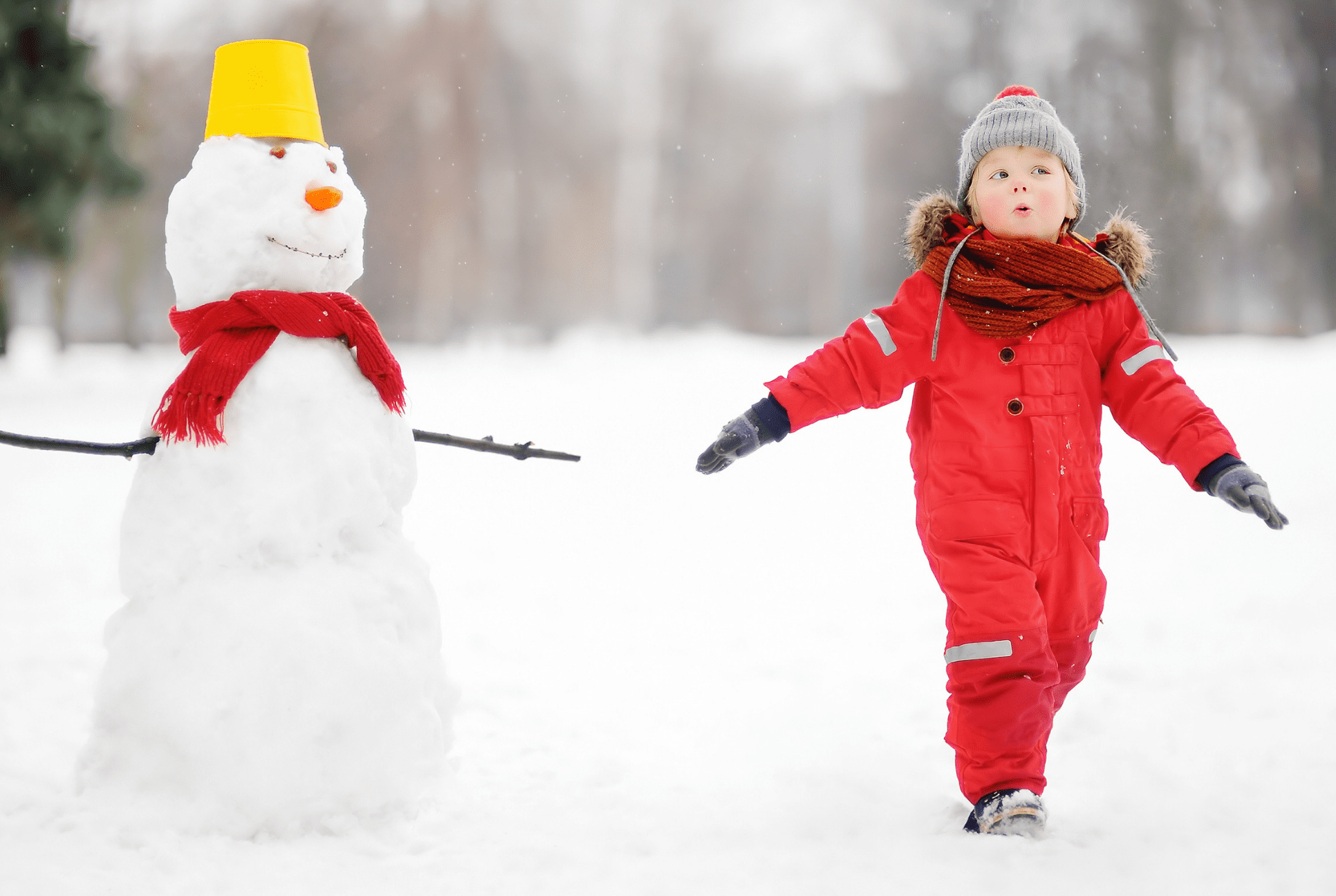 boy in red snow suit next to snowman