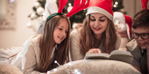 young girl and mother in funny christmas hats reading together