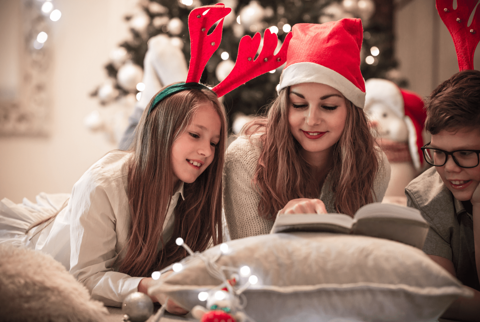 young girl and mother in funny christmas hats reading together