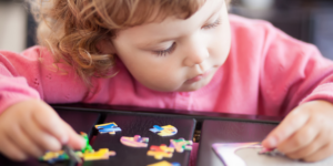 toddler in pink shirt putting puzzle pieces together
