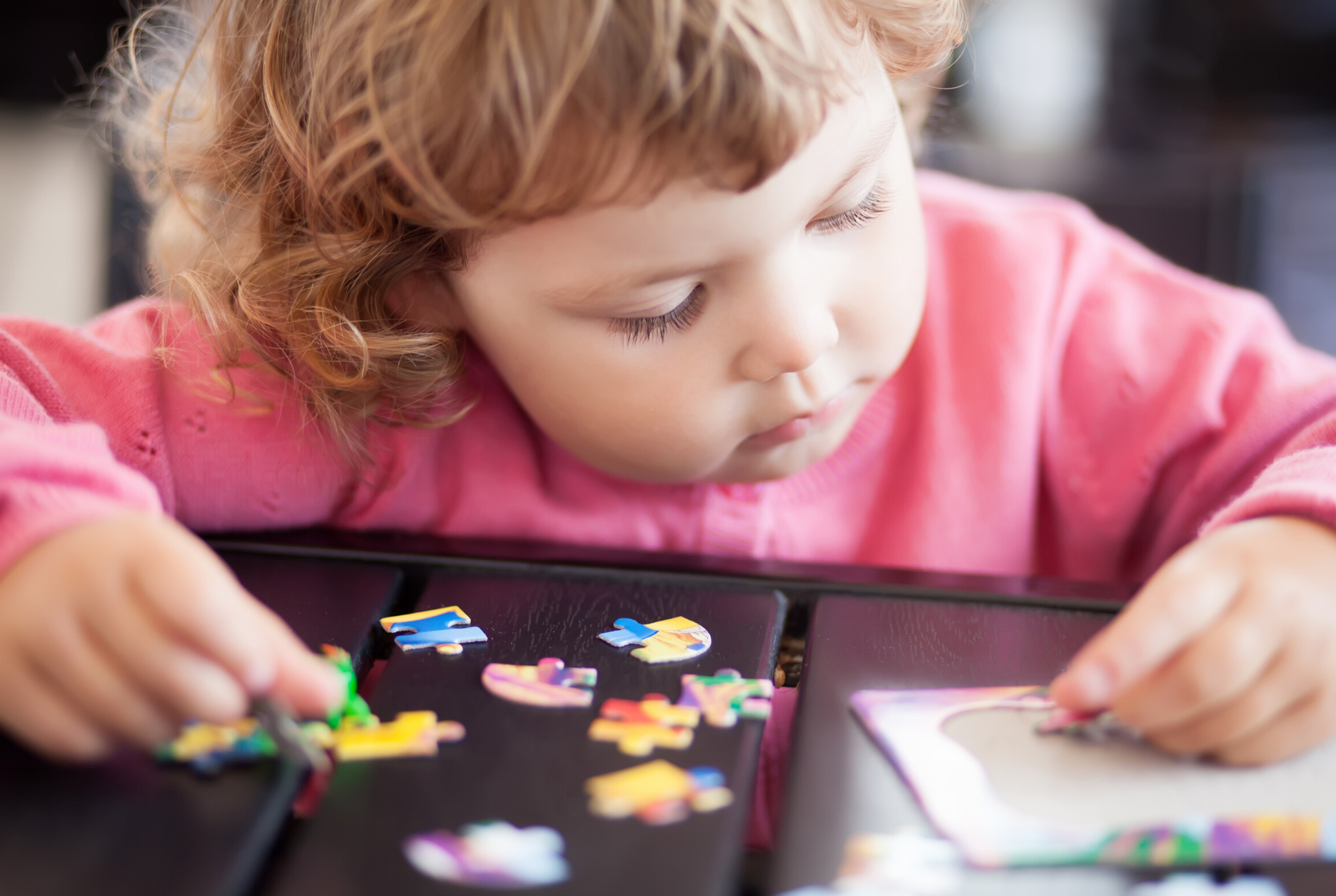 toddler in pink shirt putting puzzle pieces together