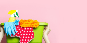 pink background with green bucket full of colorful cleaning supplies