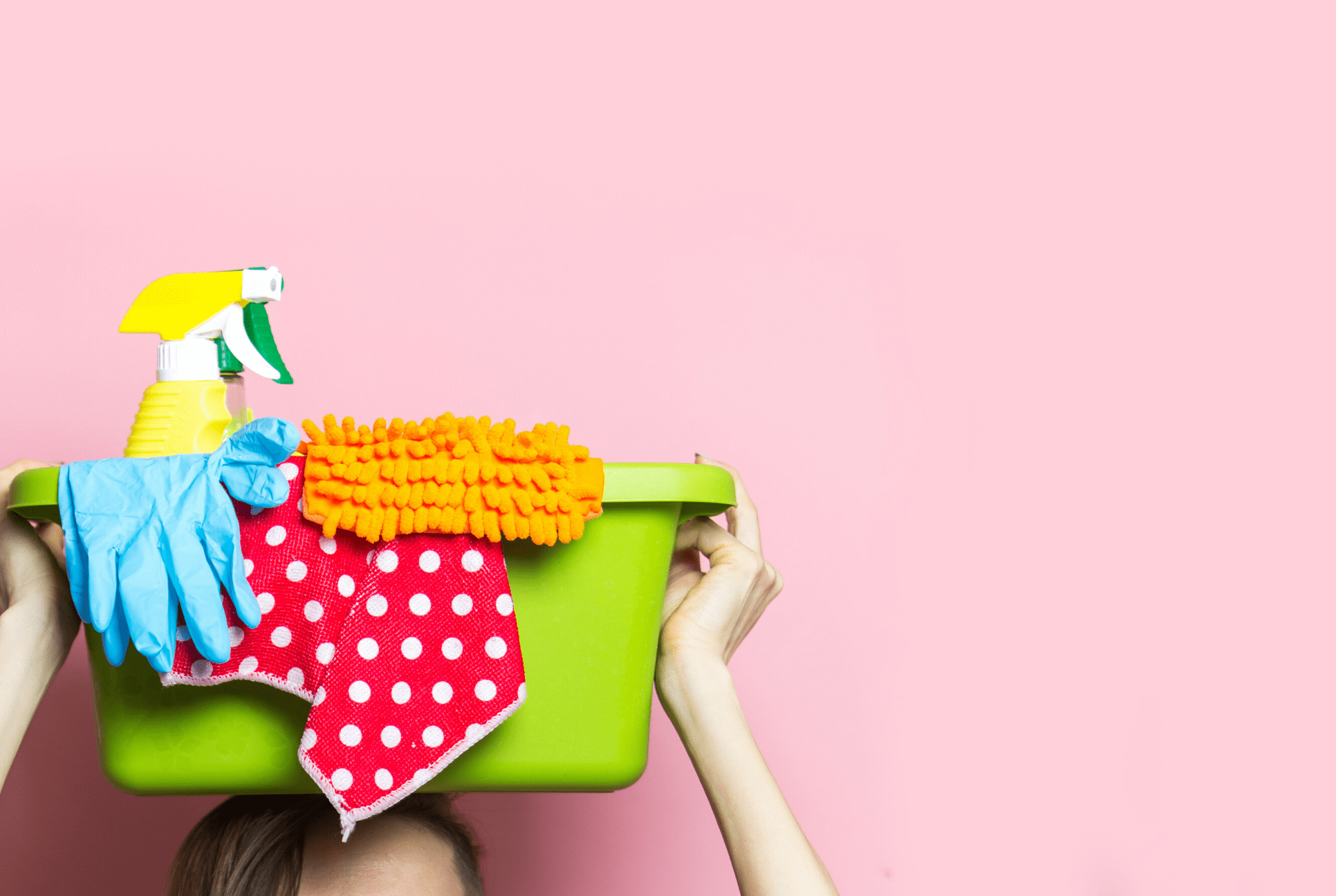 pink background with green bucket full of colorful cleaning supplies