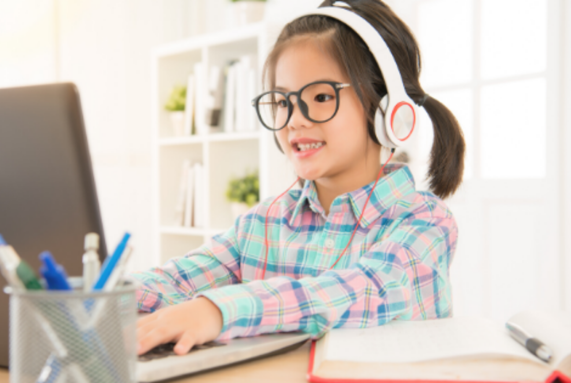young child wears headphones and works on a laptop