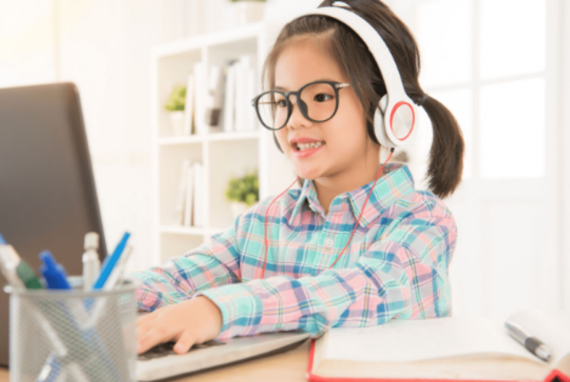 young child wears headphones and works on a laptop