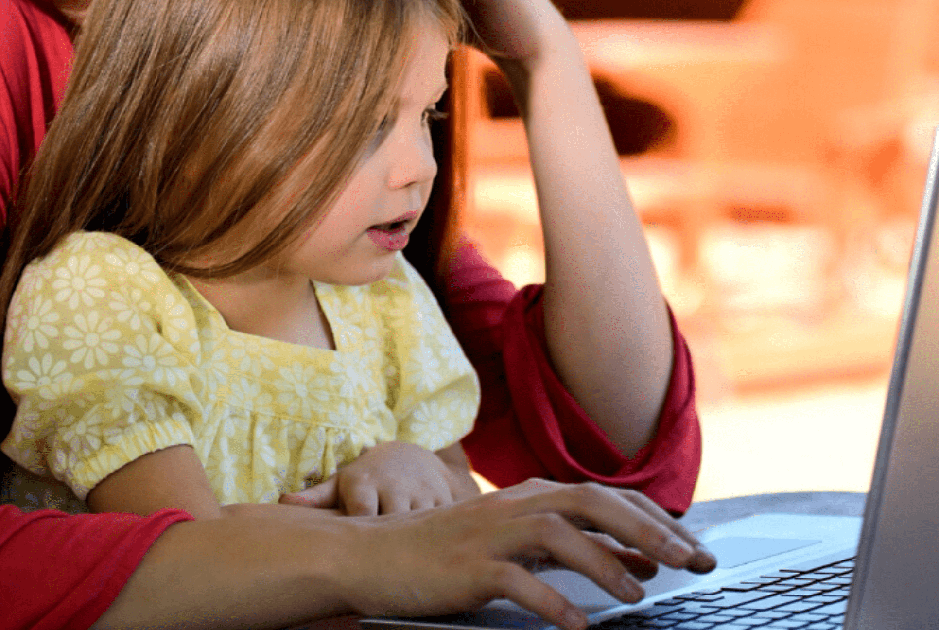 young girl sits on her parent's lap looking at a laptop